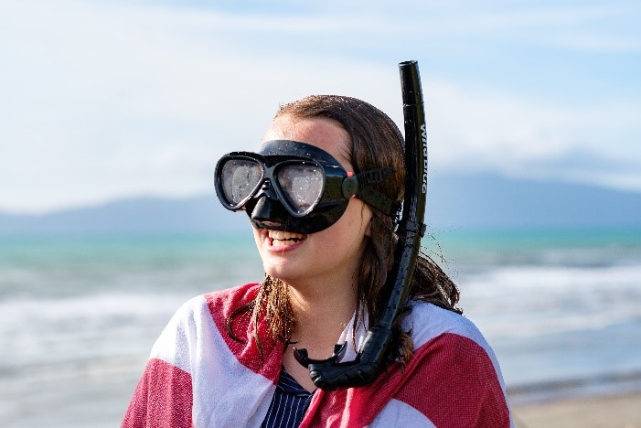 A smiling child on a beach, wearing a snorkel and googles and a towel around their shoulders