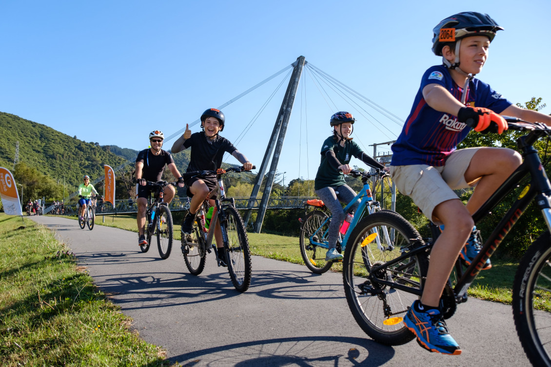 A line of cyclists bike down a path - a boy smiles and gives a thumbs up to the camera