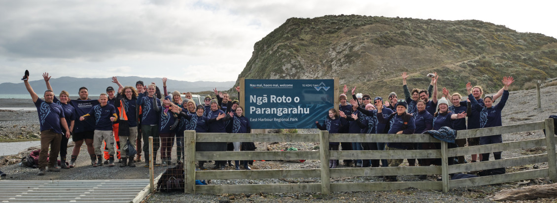 Attendees wearing the new T-shirts gather around a new welcome sign for the Parangarahu Lakes, which also features the tohu