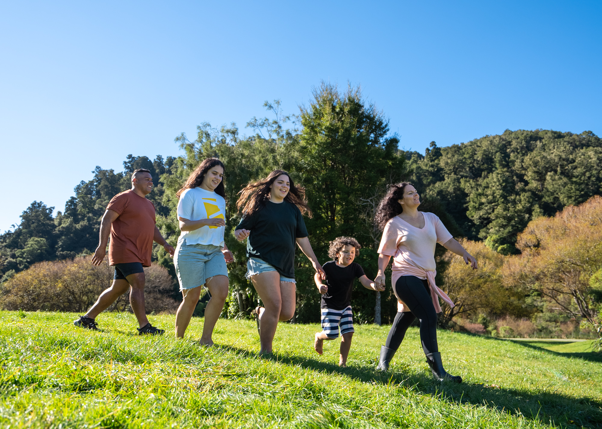 A family of five walks down a grassy hill in the sunshine