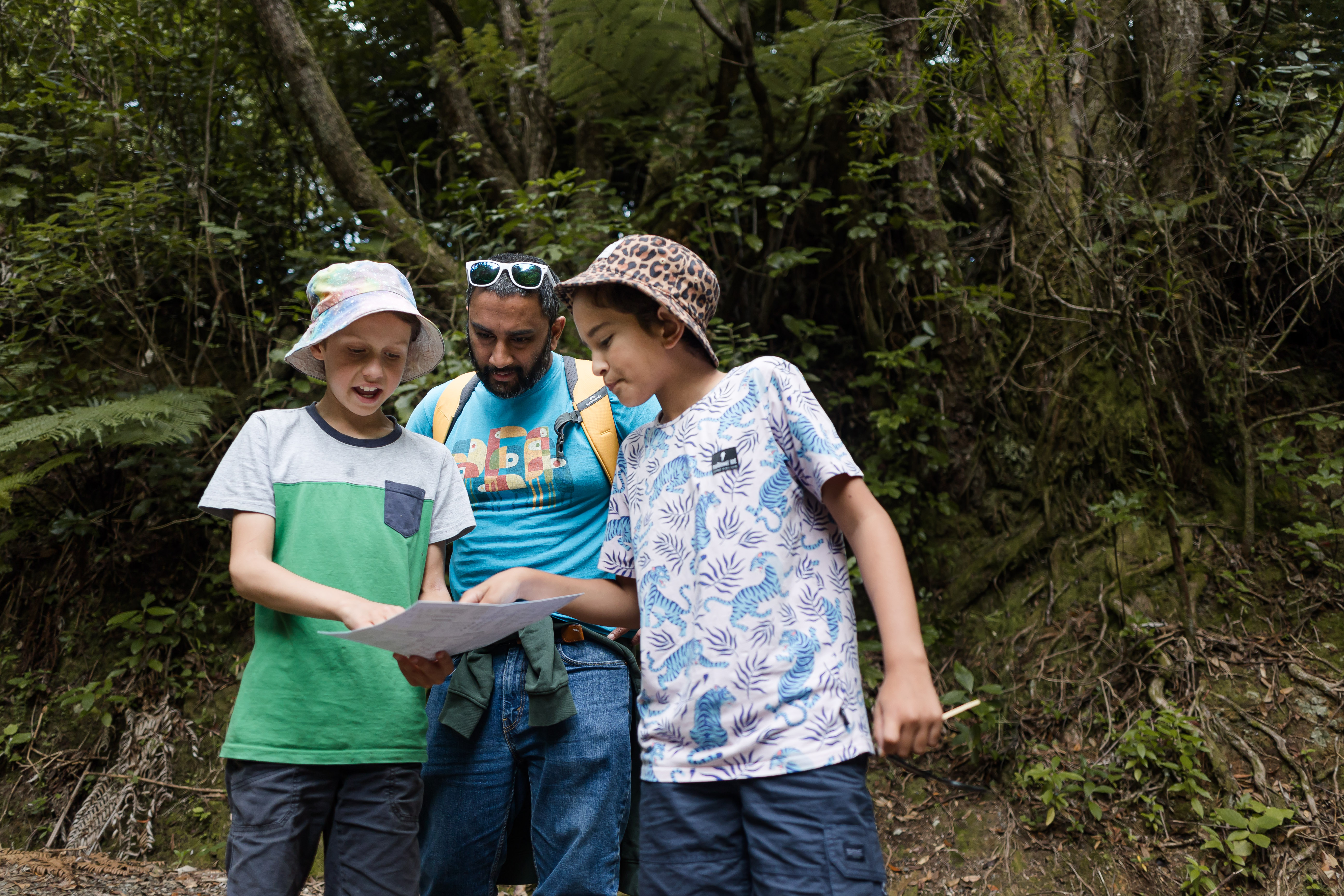Two children and an adult stand in a sunny forest and consult a map