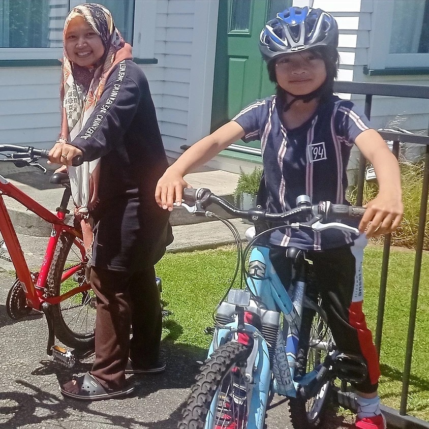 A child on a bike and a woman next to a bike smile at the camera