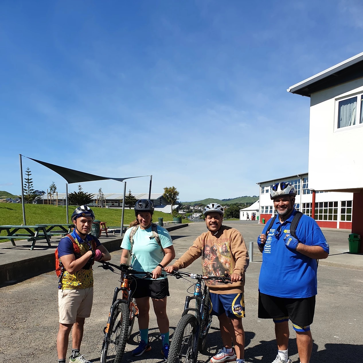 Four people in bike helmets, two with bikes, smile at the camera