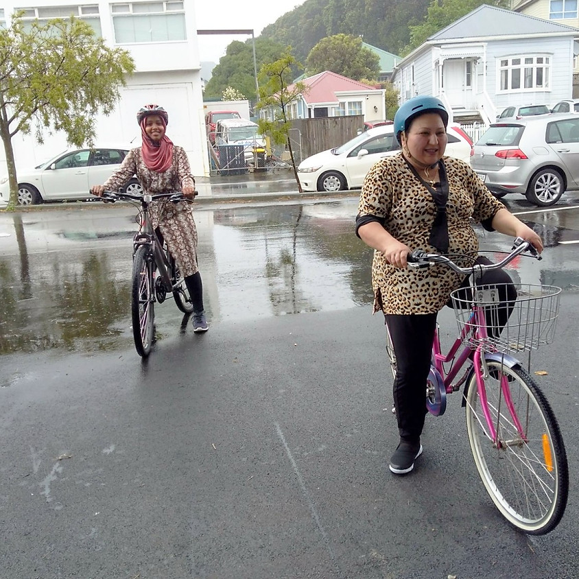 Two women sit on bikes and smile at the camera