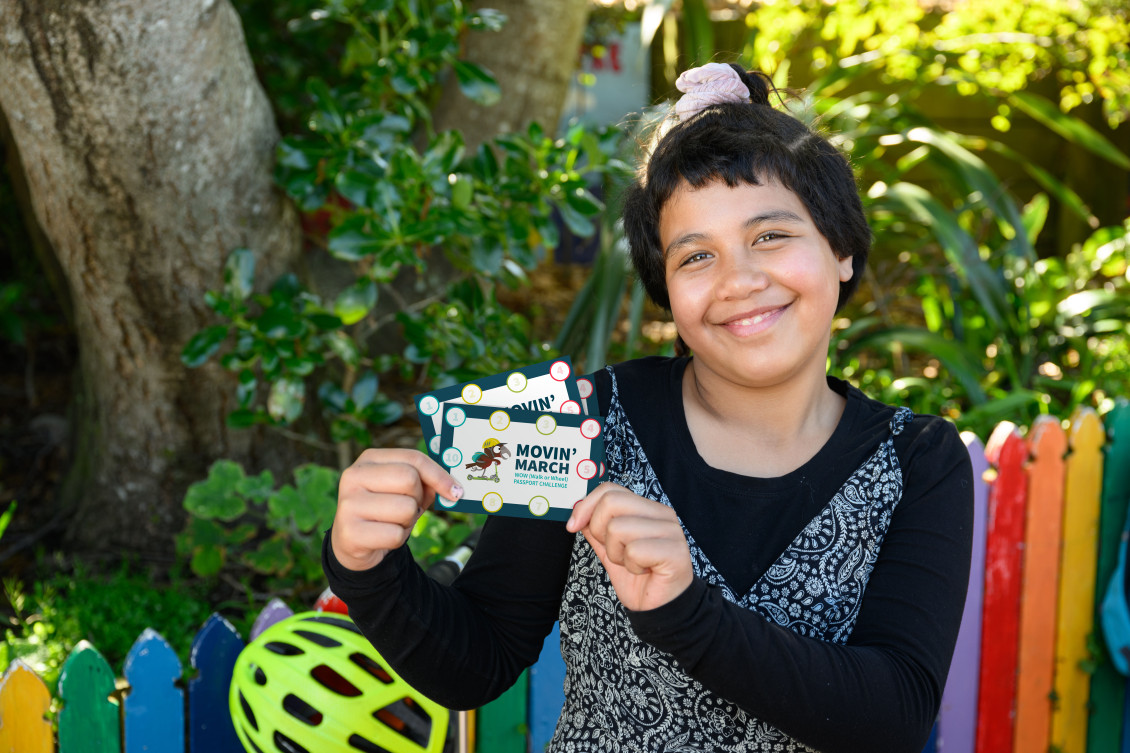 A girl smiles and holds up Movin'March walk or wheel passports