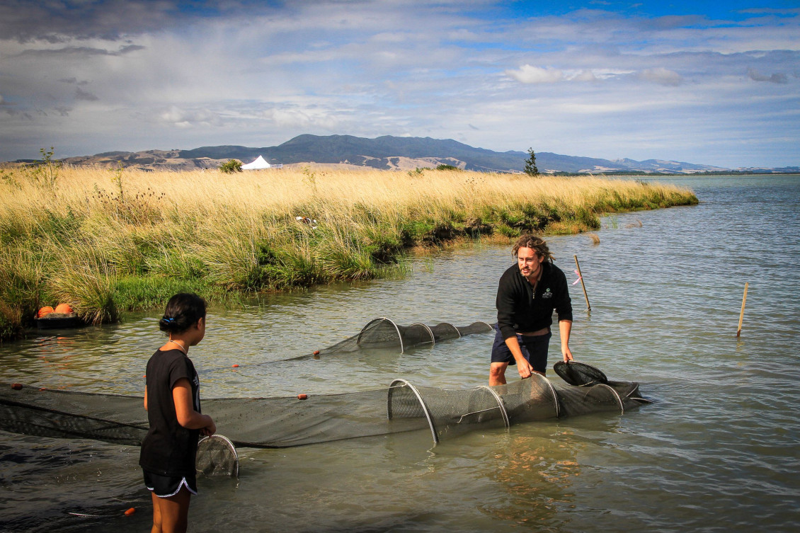 A man wades next to a net in Wairarapa Moana, talking to a child in shallower water