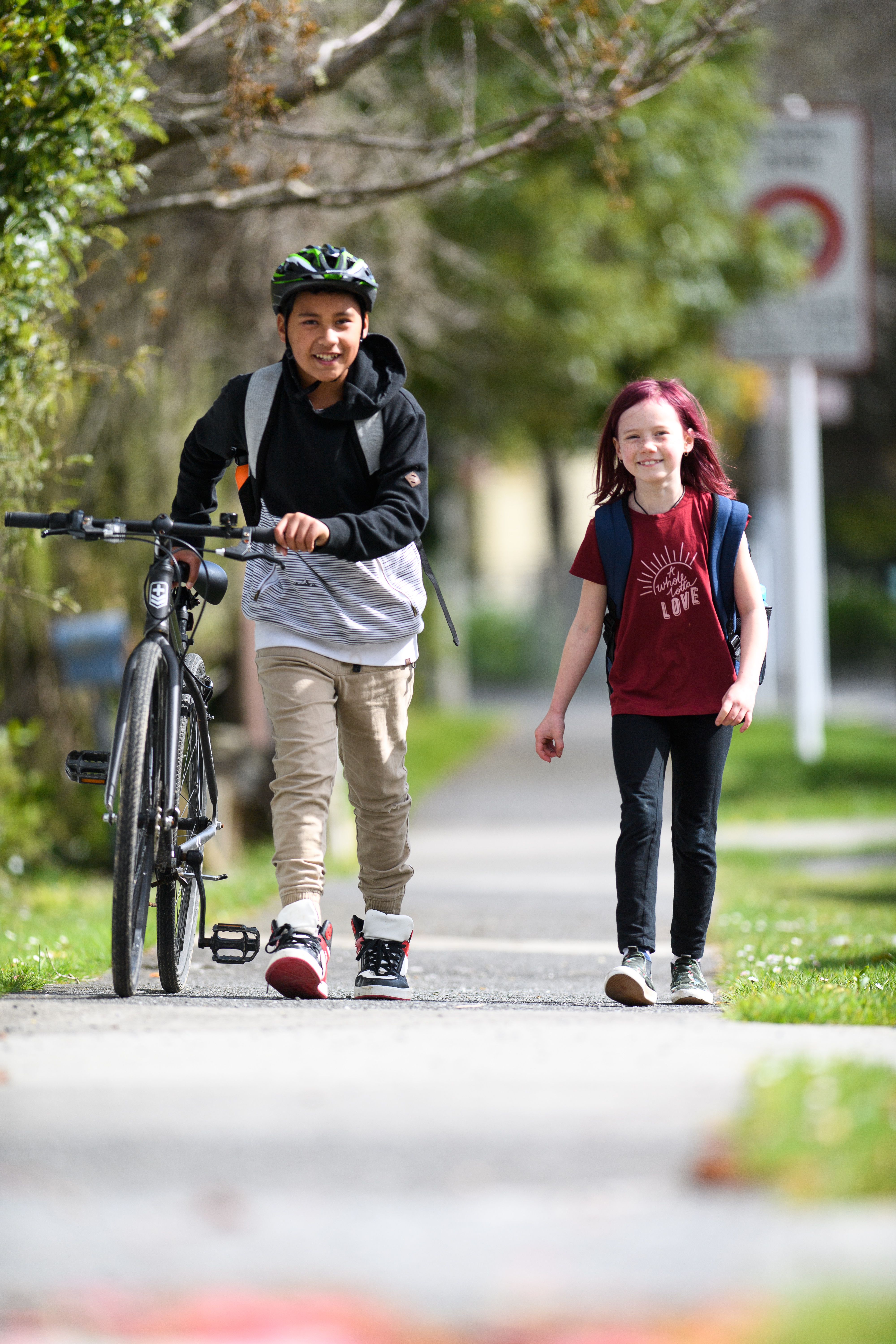 Two schoolchildren smiling and walking down a footpath