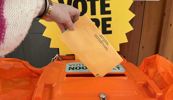 A hand holding voting papers about to drop them in a voting box
